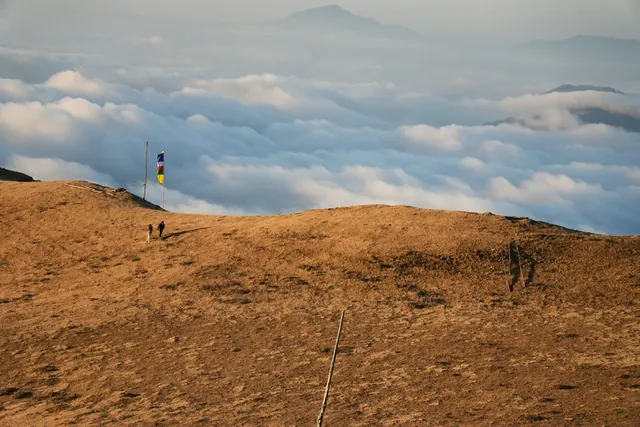 Two trekkers on a golden grass ridge below a prayer flag, with a sea of clouds beyond, Sailung