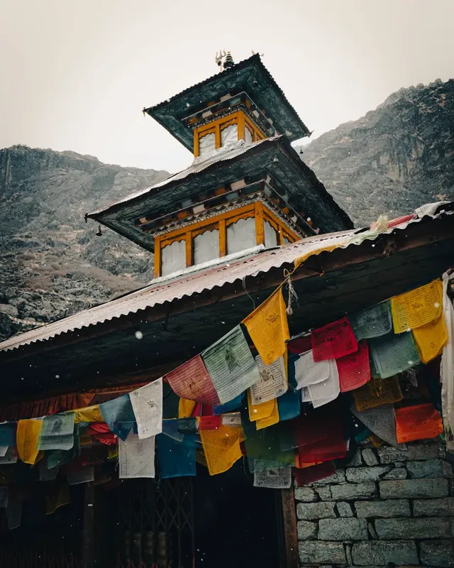 Colourful prayer flags hang below the eaves of a two-tiered temple as light snow falls, Panch Pokhari