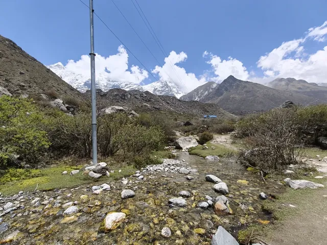 Snow-capped peaks and white clouds above a rocky, mossy stream in the Langtang valley