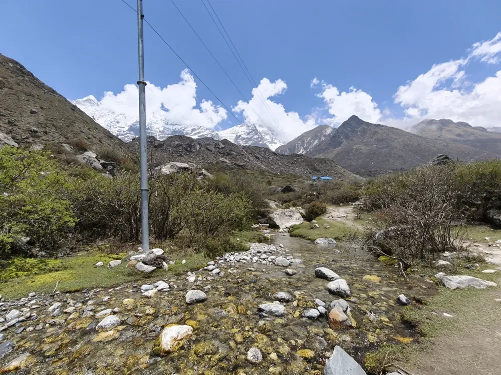 Snow-capped peaks and white clouds above a rocky, mossy stream in the Langtang valley