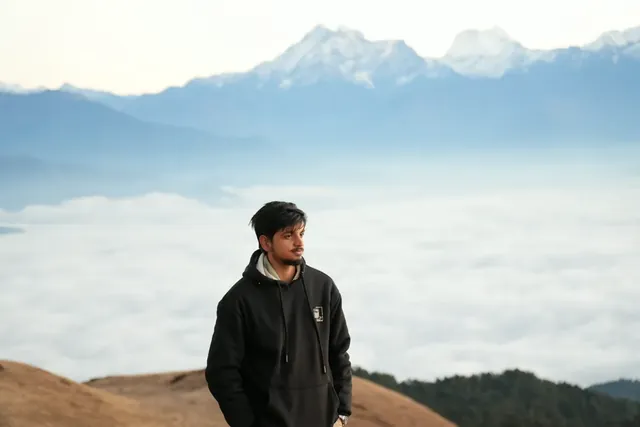 A man in a black hoodie on a grassy Sailung ridge, with a sea of cloud and snow peaks behind him