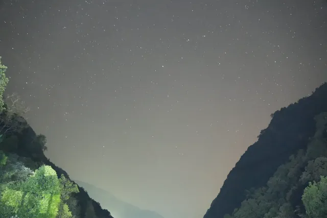 A sky full of stars above a V-shaped gap between two dark forested ridges in the Langtang valley