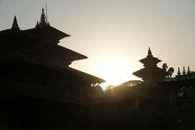 Dark silhouettes of tiered pagoda temple roofs and spires against a hazy low sun, Patan Durbar Square