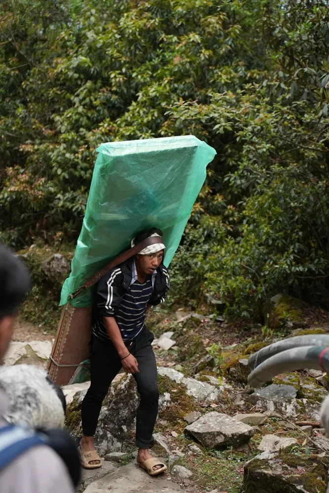 A porter carrying a large load wrapped in green plastic along the Panch Pokhari trail