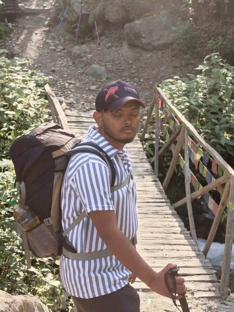 A trekker with a backpack and trekking pole stands on a wooden bridge strung with prayer flags, Langtang valley