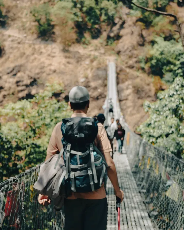 A trekker seen from behind crosses a long suspension bridge on the Panch Pokhari trail