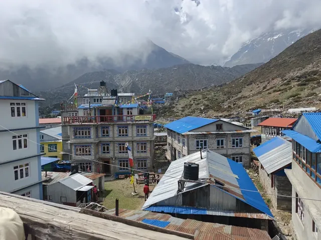 Metal-roofed lodges and prayer flags in the village of Kyanjin Gompa, with cloud-covered mountains behind