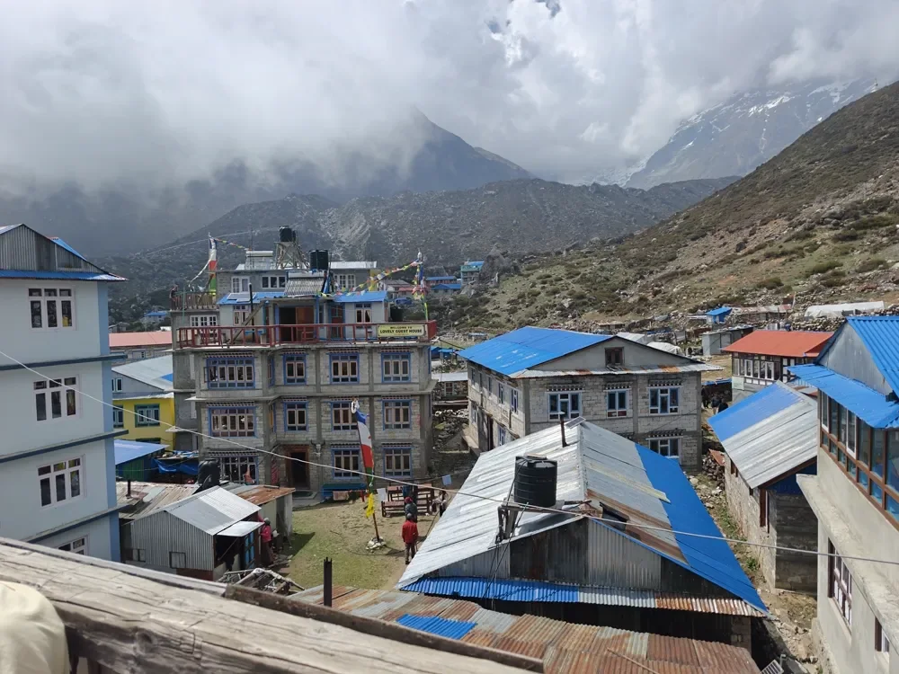 Metal-roofed lodges and prayer flags in the village of Kyanjin Gompa, with cloud-covered mountains behind